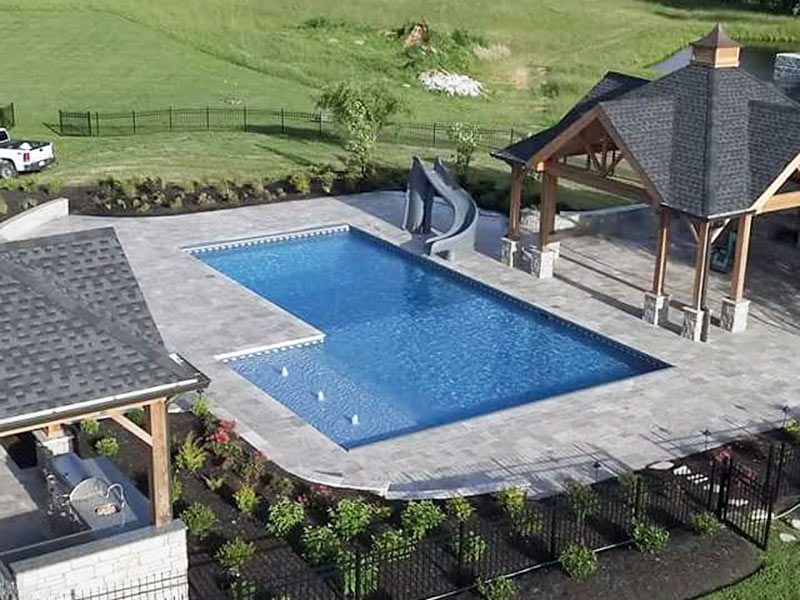 L-shaped pool with a slide in a backyard.