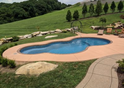 Asymmetric pool in an unfenced backyard with a beautiful lawn view.