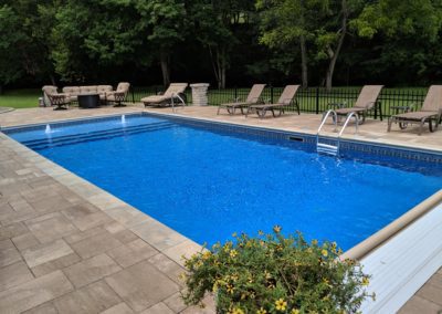 Rectangular pool with steps and lounge chairs.