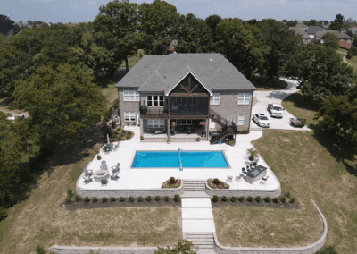 A Birdseye view of a big two-story house with a rectangular backyard pool, an outdoor fireplace and BBQ grill.